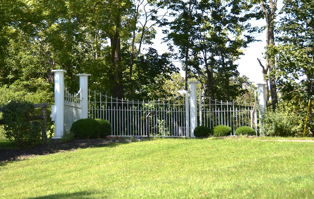 A well-maintained white fence entrance surrounded by greenery on a sunny day.